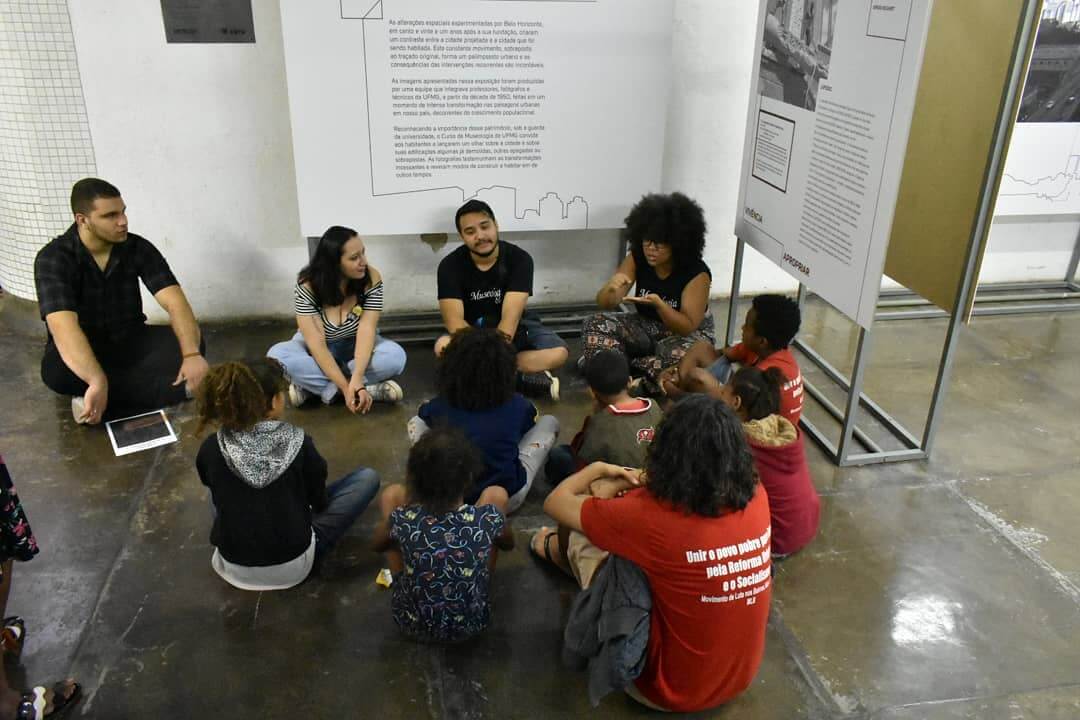 Uma roda de jovens conversam sentados no chão, na exposição no Metrô de BH.